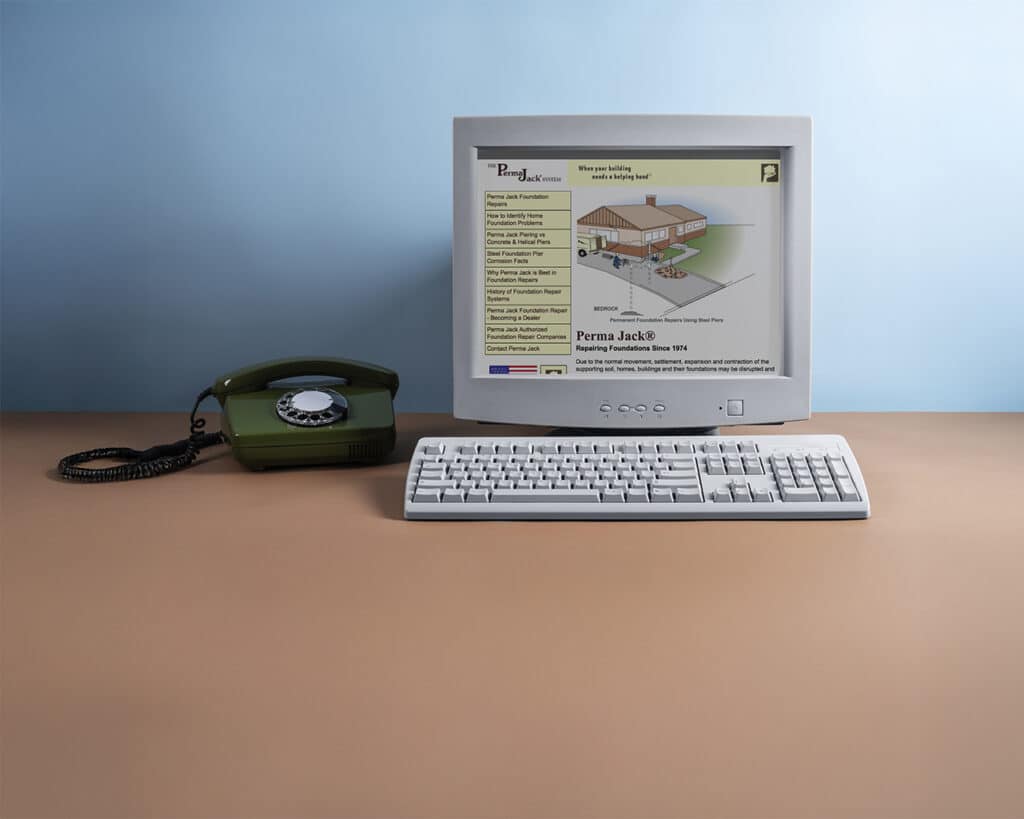 Retro computer setup with an old monitor, keyboard, and rotary phone displaying the Perma Jack website from the early internet era.