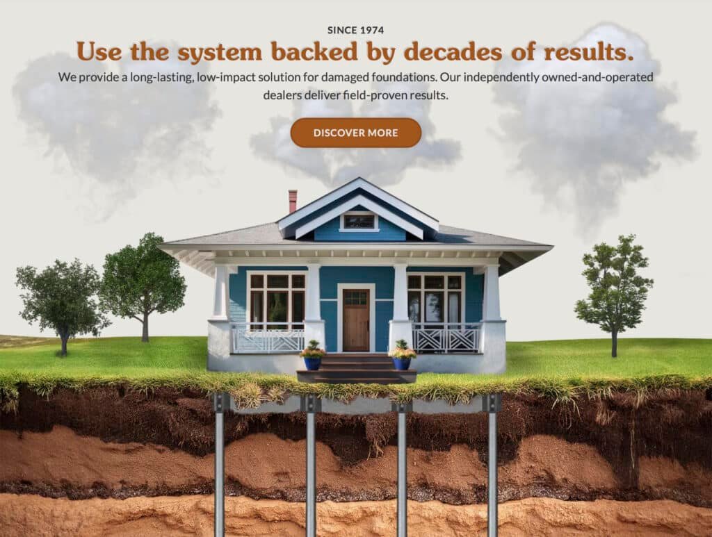 Screenshot of the current Perma Jack website's homepage hero section. At the top, a "Since 1974" label introduces the headline "Use the system backed by decades of results," with supporting text about Perma Jack's long-lasting, low-impact foundation solution and independently owned dealers, plus an orange "Discover More" button. Below is an illustration of a blue craftsman-style bungalow with a white porch, flanked by trees and clouds, shown with a cross-section cutaway of the ground revealing several metal Perma Jack piers driven down through layered soil strata to support the foundation.