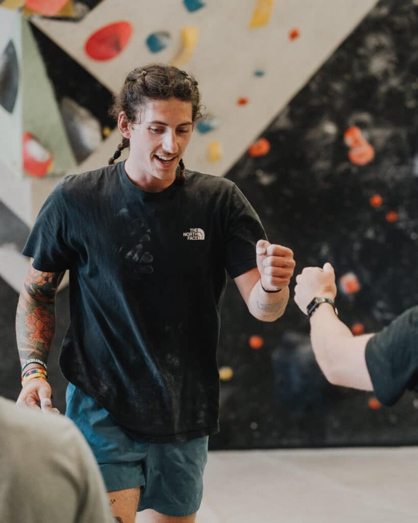 Fist bump between two climbers at Climb So iLL bouldering gym, colorful climbing holds on the wall behind them.