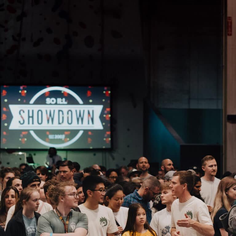 A dense crowd gathers beneath a large screen displaying a "So iLL Showdown" logo at a climbing competition event, with a bouldering wall visible above the screen.